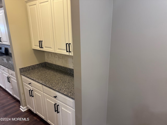 kitchen featuring white cabinets, dark stone countertops, dark wood-type flooring, and backsplash