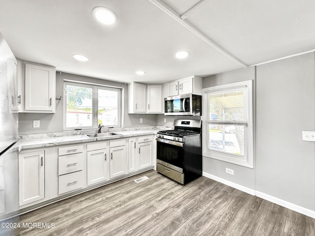 kitchen featuring light hardwood / wood-style floors, sink, white cabinetry, stainless steel appliances, and light stone countertops