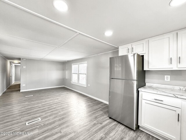 kitchen with stainless steel refrigerator, light hardwood / wood-style floors, light stone counters, and white cabinets