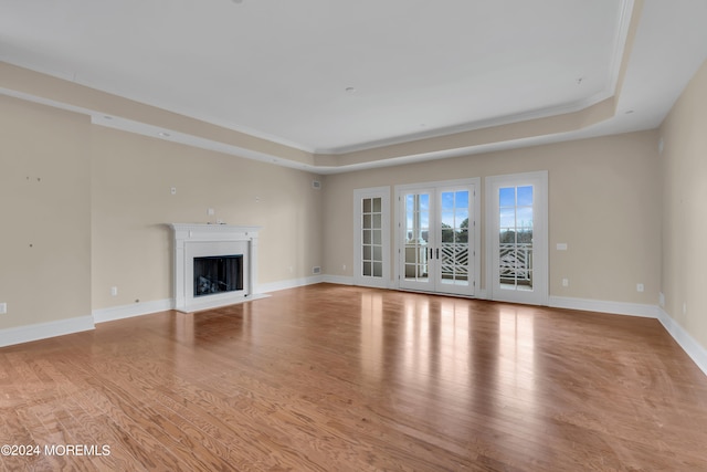 unfurnished living room with light wood-type flooring, a raised ceiling, and crown molding