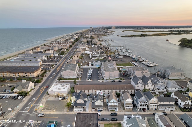 aerial view at dusk featuring a water view and a beach view