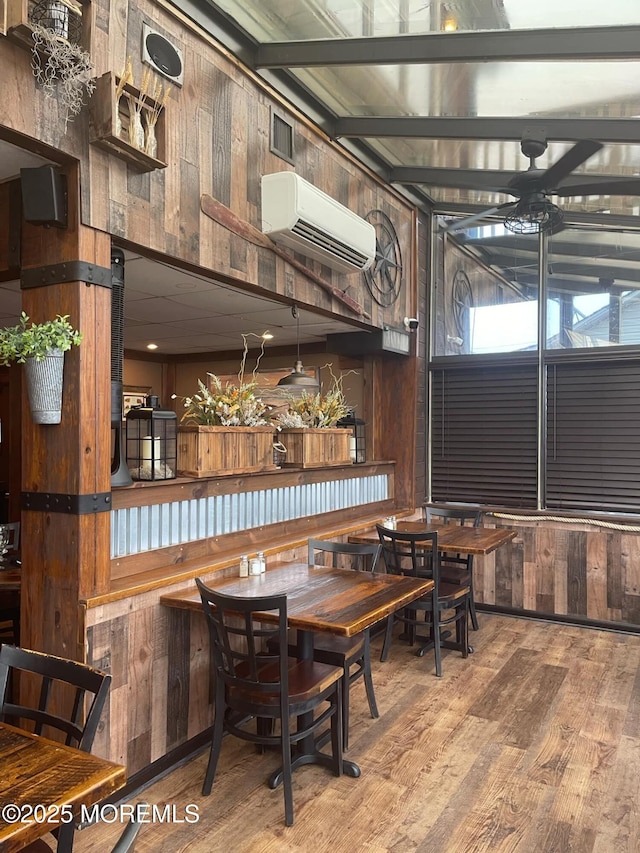 dining area with a wall unit AC, ceiling fan, wood-type flooring, and wooden walls