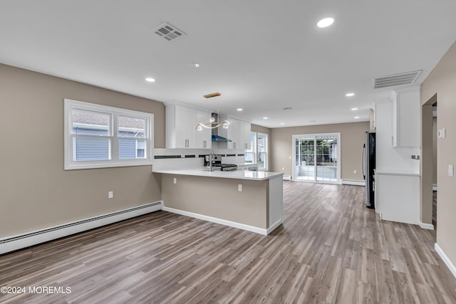 kitchen with hanging light fixtures, kitchen peninsula, white cabinetry, and wall chimney range hood