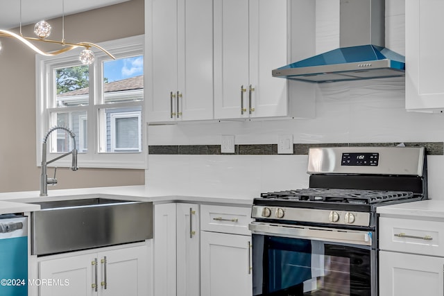 kitchen featuring wall chimney exhaust hood, white cabinets, appliances with stainless steel finishes, and decorative light fixtures