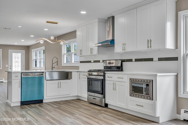 kitchen featuring stainless steel appliances, white cabinetry, plenty of natural light, and wall chimney range hood