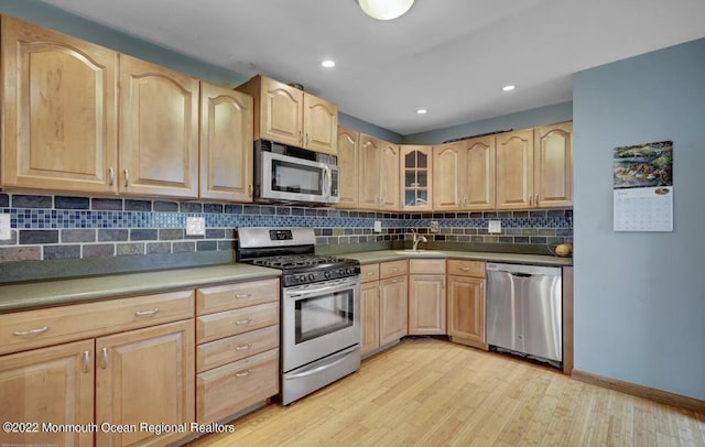 kitchen with backsplash, light brown cabinetry, light wood-type flooring, stainless steel appliances, and a sink