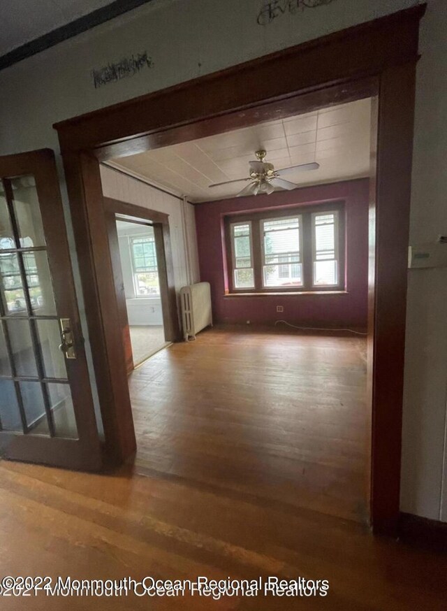 hallway with radiator heating unit, a healthy amount of sunlight, and wood-type flooring