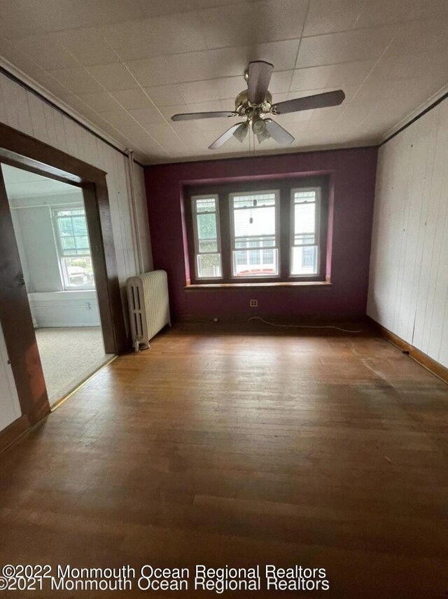 empty room with radiator heating unit, hardwood / wood-style floors, ceiling fan, and wooden walls