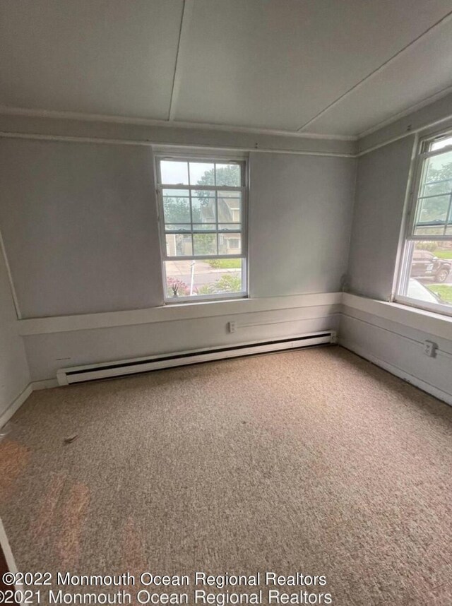 carpeted empty room with a baseboard heating unit and plenty of natural light