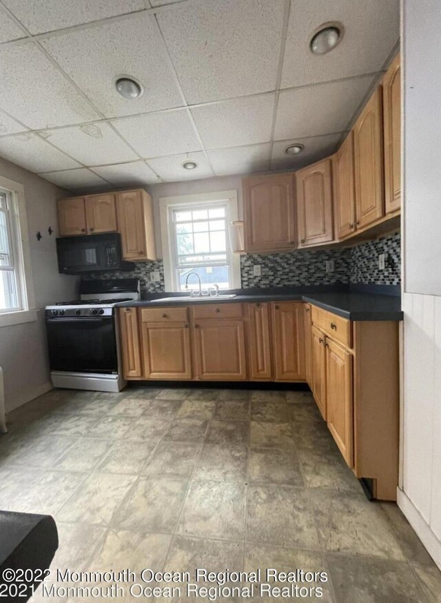 kitchen featuring a paneled ceiling, range with gas stovetop, tasteful backsplash, and sink