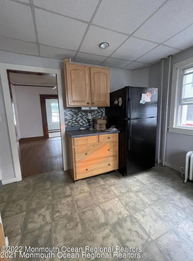 kitchen featuring black fridge, a paneled ceiling, and backsplash