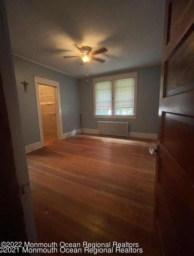 empty room featuring radiator, wood-type flooring, and ceiling fan