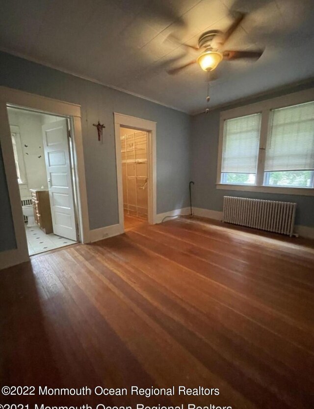 interior space with radiator heating unit, hardwood / wood-style floors, ceiling fan, and a walk in closet