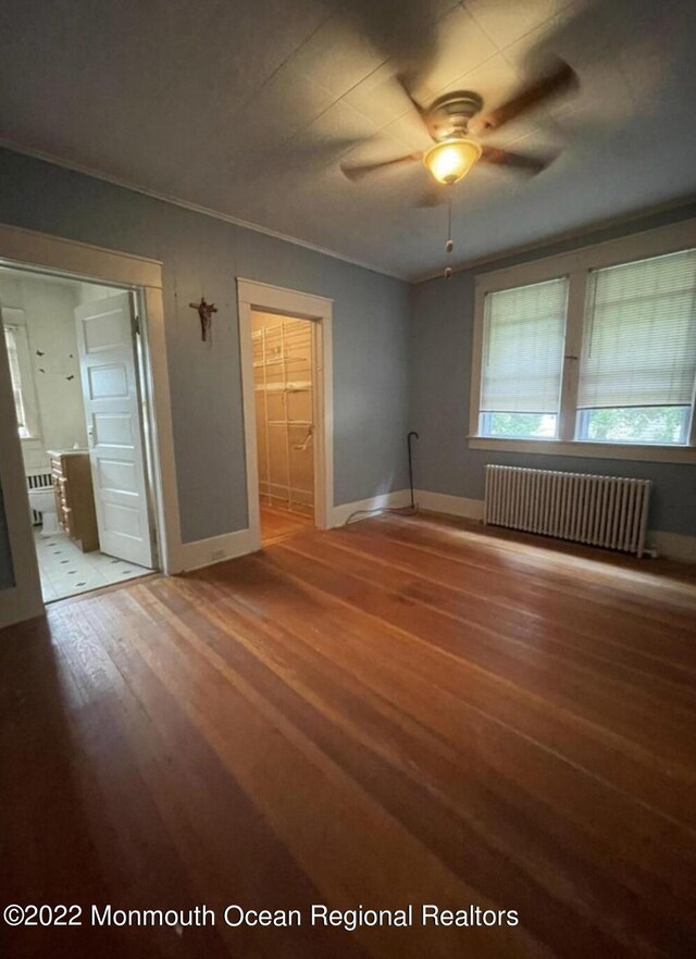 empty room featuring ceiling fan, hardwood / wood-style flooring, and radiator heating unit