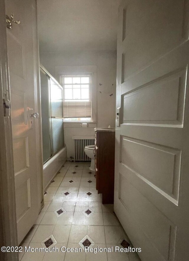 full bathroom featuring vanity, toilet, radiator heating unit, and bath / shower combo with glass door