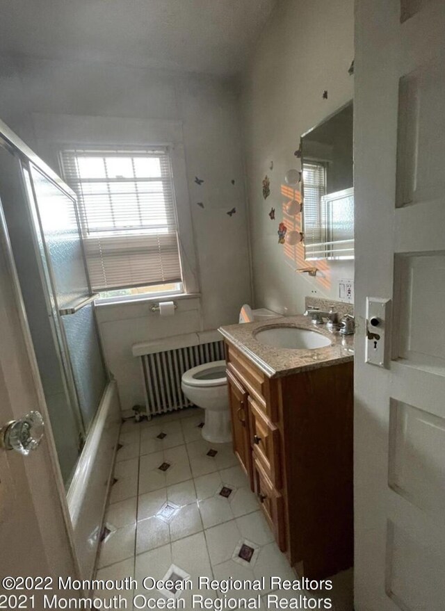 full bathroom with vanity, combined bath / shower with glass door, tile patterned flooring, toilet, and radiator heating unit