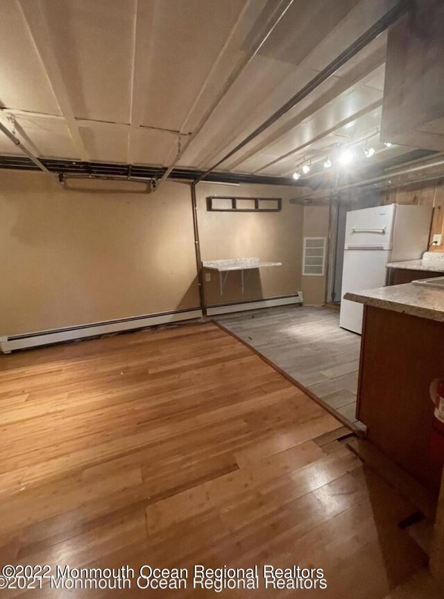 basement featuring light wood-type flooring, white refrigerator, and a baseboard radiator