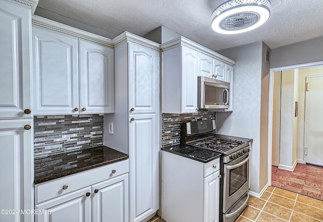 kitchen featuring light tile patterned floors, stainless steel appliances, white cabinetry, decorative backsplash, and a textured ceiling