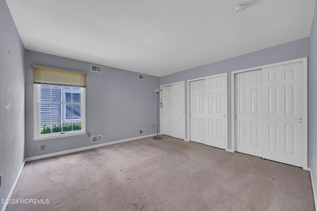 unfurnished bedroom featuring light carpet and two closets