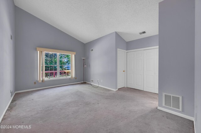 interior space featuring a closet, high vaulted ceiling, light colored carpet, and a textured ceiling