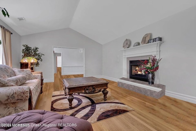 living room featuring a tile fireplace, lofted ceiling, and light hardwood / wood-style flooring