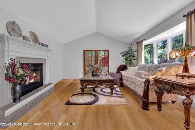 living room featuring light wood-type flooring, lofted ceiling, and a tiled fireplace