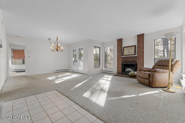 unfurnished living room with light carpet, a baseboard heating unit, a wealth of natural light, and a brick fireplace