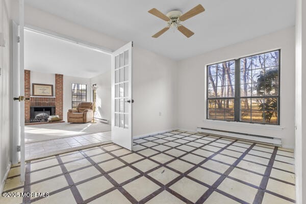 unfurnished room featuring french doors, ceiling fan, a brick fireplace, and a baseboard heating unit