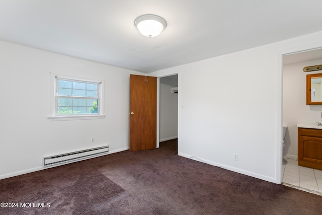 unfurnished bedroom with dark colored carpet, baseboard heating, and ensuite bathroom