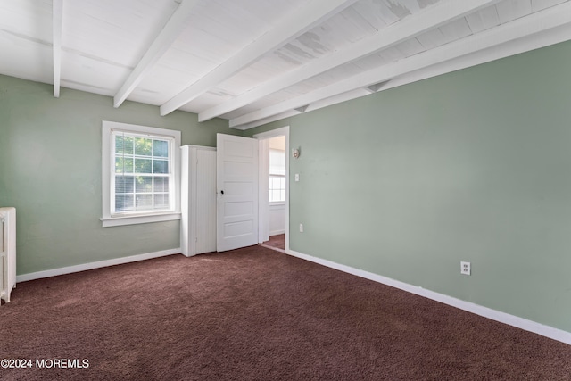 empty room with dark carpet, radiator, and beamed ceiling