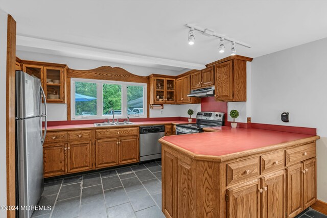 kitchen with dark tile patterned floors, kitchen peninsula, sink, and appliances with stainless steel finishes