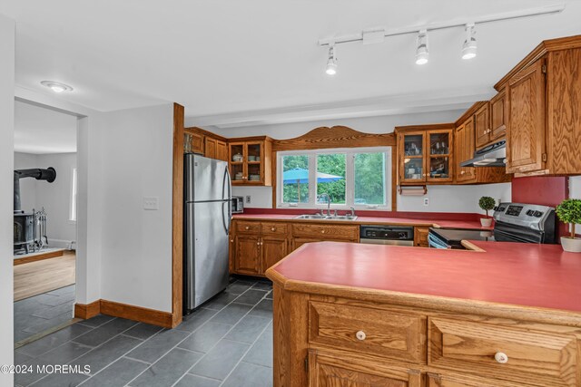 kitchen with dark tile patterned floors, a wood stove, stainless steel appliances, sink, and rail lighting