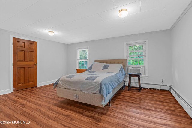 bedroom featuring multiple windows, wood-type flooring, a baseboard heating unit, and ornamental molding