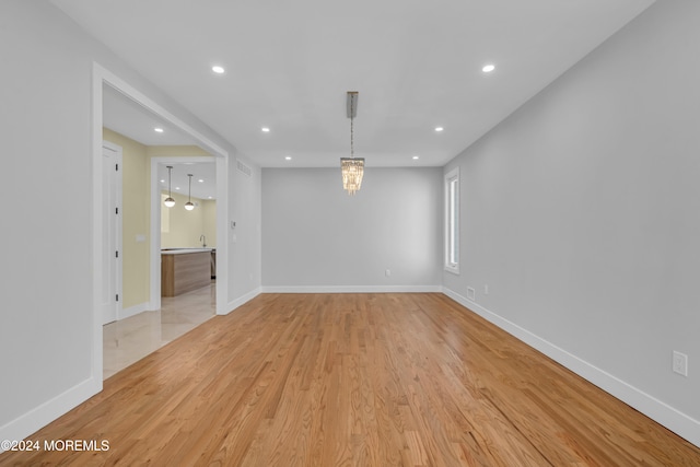 empty room with light hardwood / wood-style flooring and an inviting chandelier