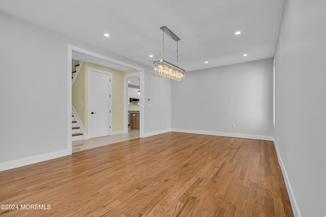 unfurnished room featuring an inviting chandelier and light wood-type flooring