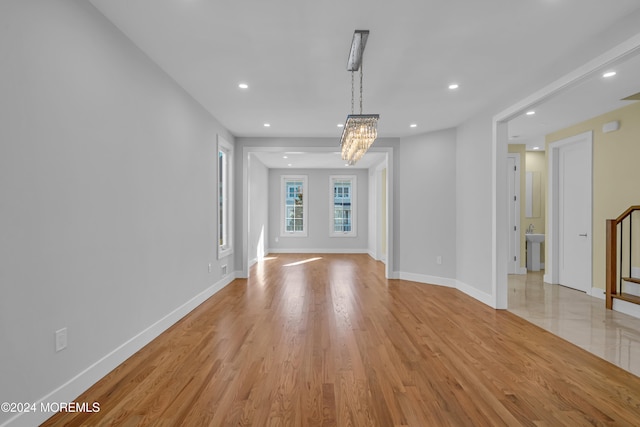 unfurnished living room with an inviting chandelier, sink, and light hardwood / wood-style floors