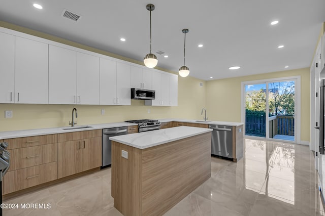 kitchen with sink, a kitchen island, white cabinetry, stainless steel appliances, and decorative light fixtures