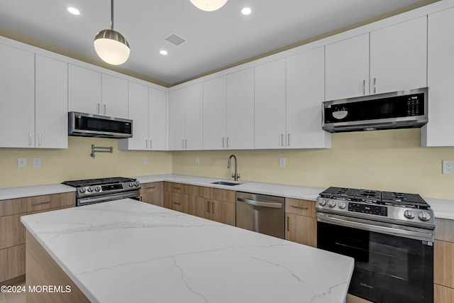 kitchen featuring light stone countertops, appliances with stainless steel finishes, sink, pendant lighting, and white cabinets