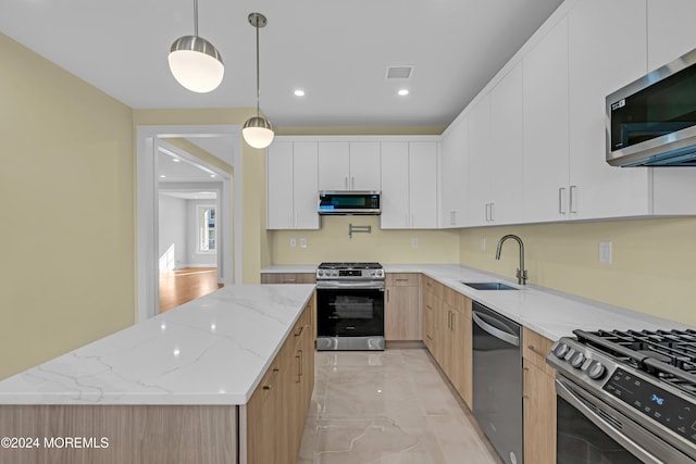 kitchen with stainless steel appliances, sink, light stone countertops, pendant lighting, and white cabinets