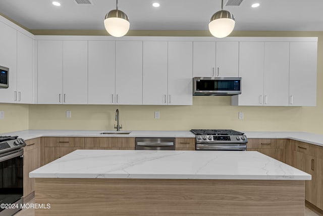 kitchen with appliances with stainless steel finishes, white cabinetry, and hanging light fixtures