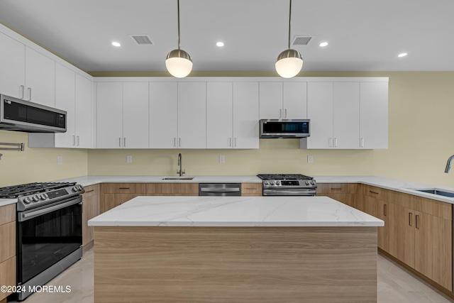 kitchen with appliances with stainless steel finishes, light stone counters, white cabinets, and hanging light fixtures