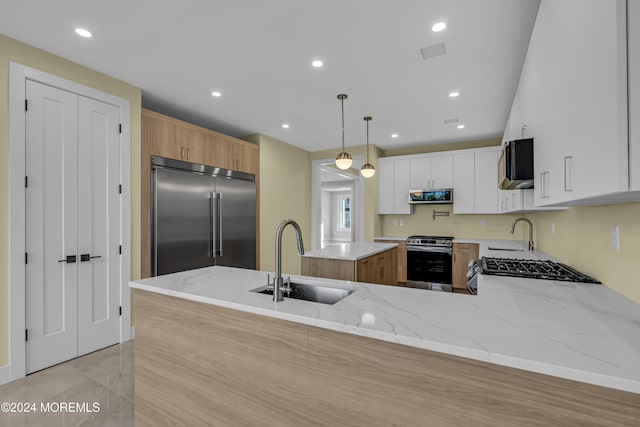 kitchen with light stone counters, white cabinetry, sink, pendant lighting, and stainless steel appliances