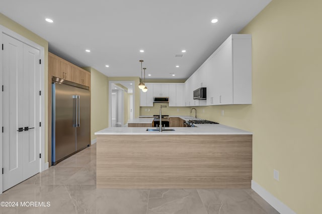 kitchen with kitchen peninsula, light brown cabinets, appliances with stainless steel finishes, white cabinetry, and pendant lighting