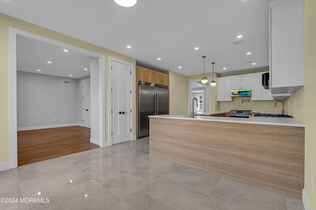 kitchen with kitchen peninsula, white cabinets, light wood-type flooring, stainless steel appliances, and decorative light fixtures