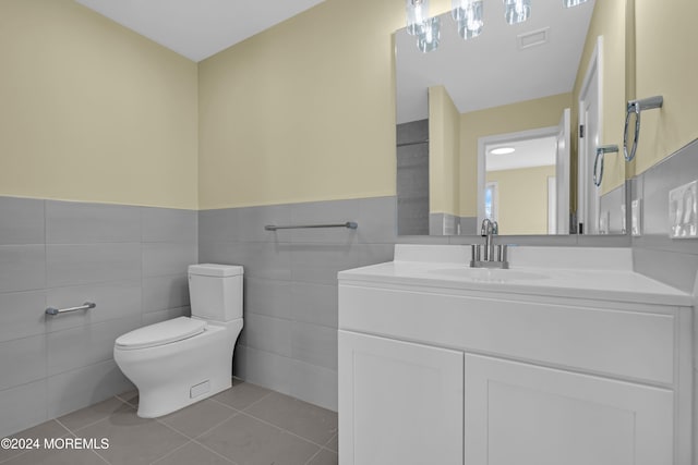 bathroom with toilet, vanity, tile patterned floors, and tile walls