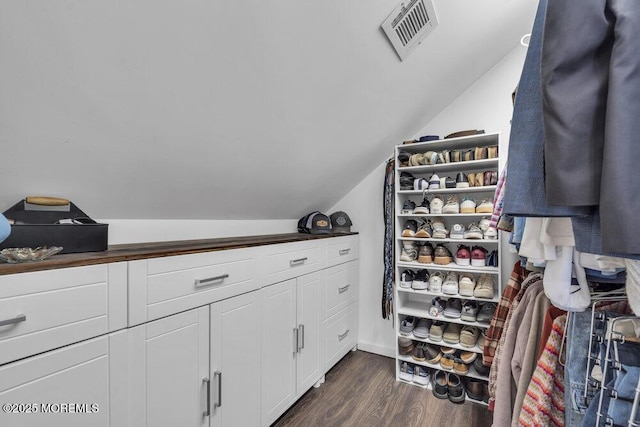 spacious closet with dark wood-style flooring, visible vents, and vaulted ceiling