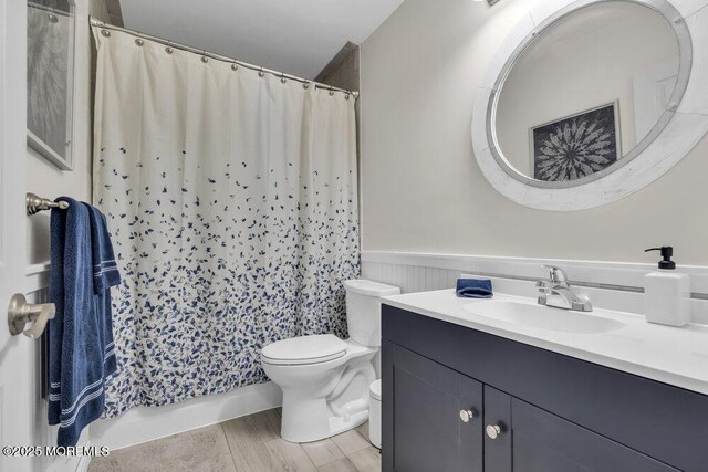 full bathroom with a shower with curtain, a wainscoted wall, vanity, and toilet