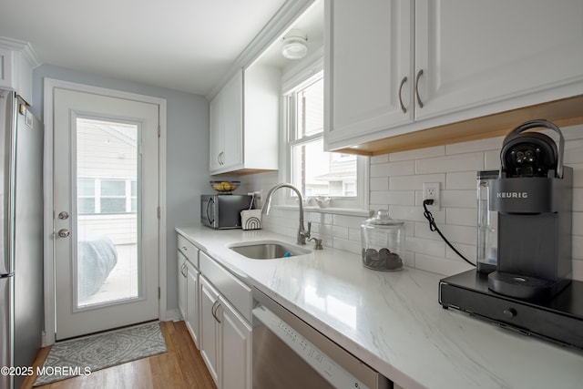 kitchen featuring stainless steel appliances, a sink, white cabinetry, decorative backsplash, and light wood-style floors