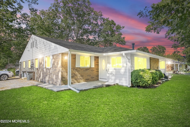 back house at dusk featuring a lawn