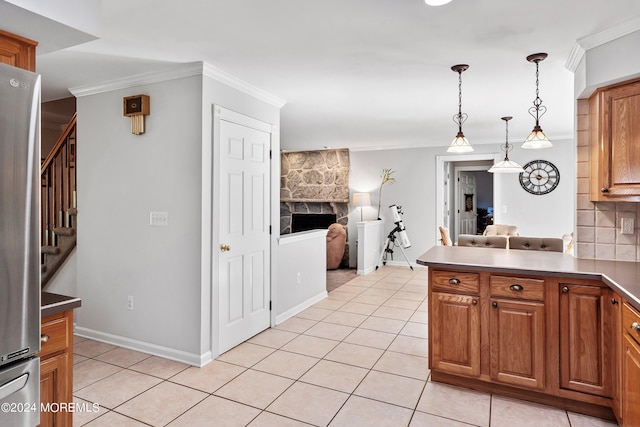 kitchen featuring light tile patterned flooring, stainless steel refrigerator, decorative light fixtures, a stone fireplace, and ornamental molding